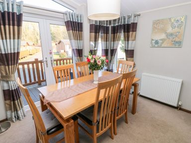A dining room with a wooden table and six chairs with a flower vase on the table at Serendipity - Heritage Park in Stepaside near Kilgetty