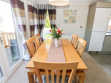 A dining area with a wooden table and six chairs with a vase of flowers on the table at Serendipity - Heritage Park in Stepaside near Kilgetty
