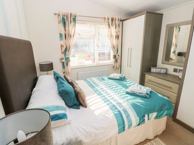 A bedroom with a bed with teal and white bedding a wardrobe with drawers and a mirror at Serendipity - Heritage Park in Stepaside near Kilgetty