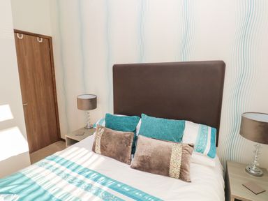 A bedroom with a bed with teal and white bedding and teal and brown pillows with two bedside tables and lamps at Serendipity - Heritage Park Stepaside near Kilgetty