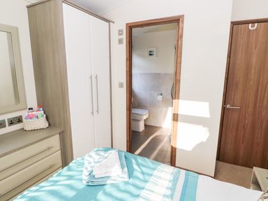 A bedroom with a bed, wardrobe, dresser with mirror, and an ensuite bathroom at Serendipity - Heritage Park Stepaside near Kilgetty