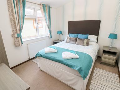 A bedroom with a double bed blue and grey pillows blue and grey bedding two bedside tables with blue lamps and a window with blue and grey curtains at Serendipity - Heritage Park Stepaside near Kilgetty