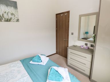A bedroom with a bed, folded towels, a dresser with a mirror, and a wooden door at Serendipity - Heritage Park Stepaside near Kilgetty