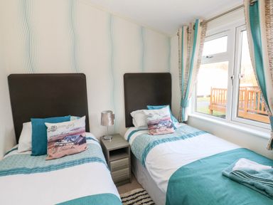 A bedroom with two single beds a small bedside table and a window with curtains at Serendipity - Heritage Park Stepaside near Kilgetty