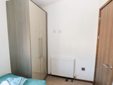 A bedroom corner with a wardrobe radiator door and part of a bed at Serendipity - Heritage Park Stepaside near Kilgetty