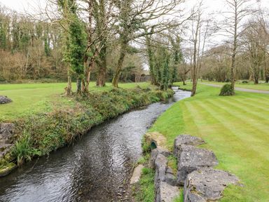 A narrow stream flowing between grassy banks and trees at Serendipity - Heritage Park in Stepaside near Kilgetty