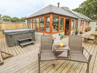 An outdoor deck with a hot tub two lounge chairs and a wooden picnic table at The Old Farm Shop in Narberth