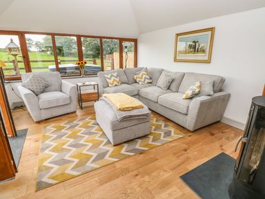A sitting area with a gray sectional sofa armchair ottoman patterned rug and wood stove at The Old Farm Shop in Narberth