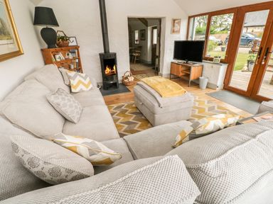 A living room with a beige sectional sofa a wood burning stove television on a stand and wooden framed glass doors at The Old Farm Shop in Narberth