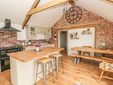 A kitchen with an island and stools a dining table and chairs and exposed brick walls at The Old Farm Shop in Narberth