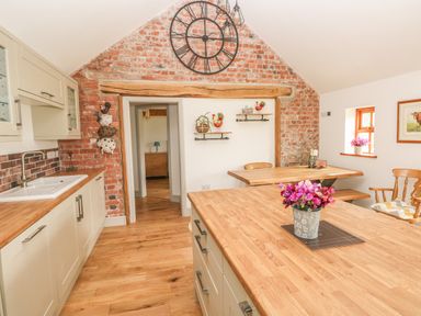 A kitchen with wooden countertops a large wall clock and a dining table at The Old Farm Shop in Narberth