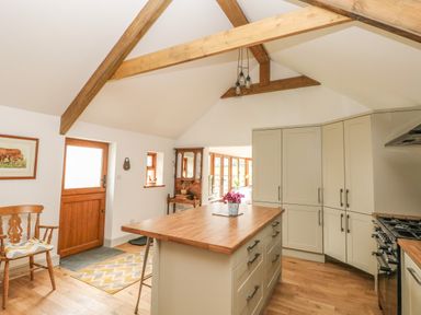 A kitchen with a wooden island and cabinets with a wooden door and chair at The Old Farm Shop in Narberth