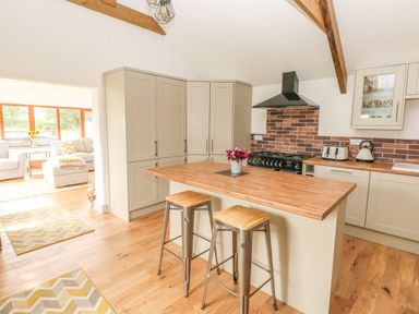 A kitchen with wooden countertops stools and appliances connected to a living area with sofas and windows at The Old Farm Shop in Narberth