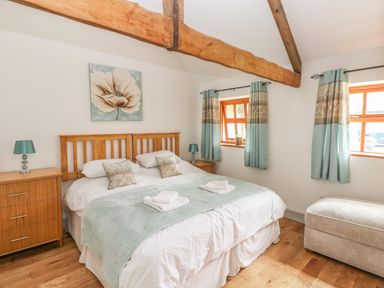 A bedroom with a wooden bed frame bedside tables lamps and windows with curtains at The Old Farm Shop in Narberth