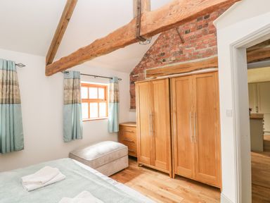 A bedroom with wooden wardrobes a window with curtains and exposed wooden beams at The Old Farm Shop in Narberth