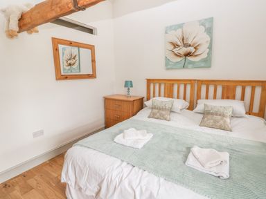 A bedroom with a double bed two pillows a bedside table with a lamp and a flower painting on the wall at The Old Farm Shop in Narberth