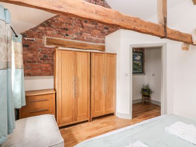 A bedroom with wooden wardrobes a chest of drawers exposed brick wall wooden ceiling beams and a doorway showing a plant at The Old Farm Shop in Narberth