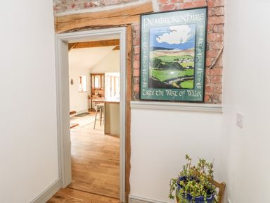 A hallway with a framed poster on a brick section of the wall and a plant in a pot by a chair at The Old Farm Shop in Narberth