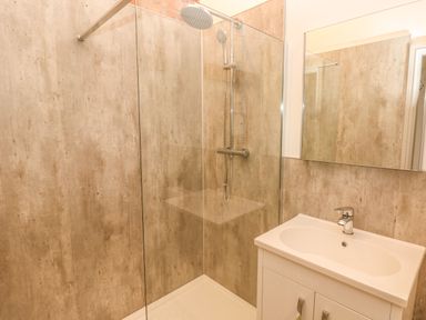 A bathroom with a shower area with glass partition, wall-mounted showerhead and a sink with cabinet at The Old Farm Shop in Narberth