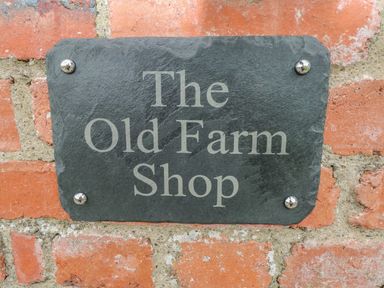 A black stone sign with the text The Old Farm Shop mounted on a brick wall at The Old Farm Shop in Narberth