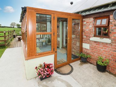 A wooden framed glass door entrance to a conservatory attached to a red brick building with potted plants outside at The Old Farm Shop in Narberth