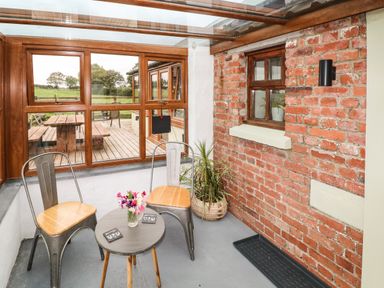 A sunroom with two metal chairs wooden seats a small round table with flowers a brick wall and a window at The Old Farm Shop in Narberth