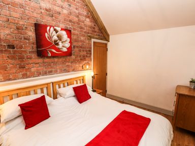 A bedroom with two single beds joined with red pillows and a red runner a wooden door and a dresser at The Old Farm Shop in Narberth