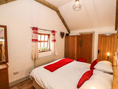 A bedroom with a bed with red pillows and blanket a wooden wardrobe and window with red and white curtains at The Old Farm Shop in Narberth