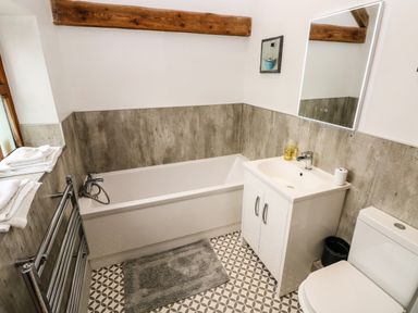 A bathroom with a bathtub sink toilet mirror and towel rack at The Old Farm Shop in Narberth