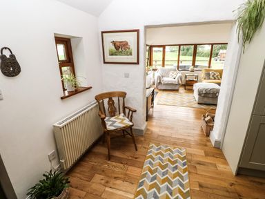 A hallway with a wooden chair and cushions and a view into a sitting room with armchairs and large windows at The Old Farm Shop in Narberth