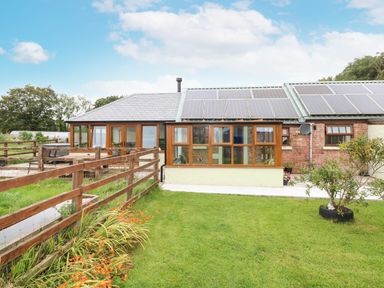 A fenced garden with a lawn and flowers in front of a house with solar panels at The Old Farm Shop in Narberth