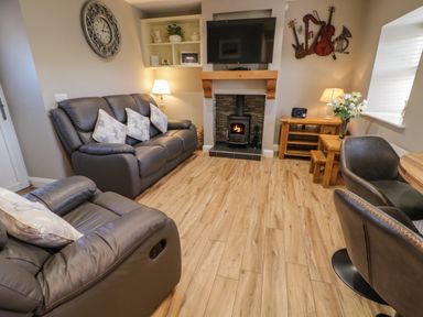 A living room with leather sofas a fireplace a wall-mounted TV a wooden floor and a small dining area at Lough Island Reavy Cottage in Kilcoo Mourne Mountains Newry County Down