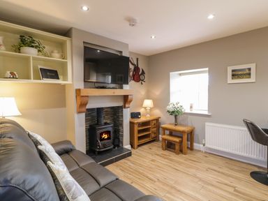 A living room with a leather sofa a wood burning stove under a mounted TV wooden furniture and a window at Lough Island Reavy Cottage in Kilcoo Mourne Mountains Newry County Down