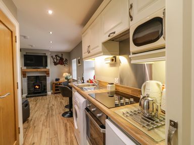 A kitchen with wooden countertops and white cabinets leading to a living area with a fireplace and wall-mounted TV at Lough Island Reavy Cottage in Kilcoo Mourne Mountains Newry County Down