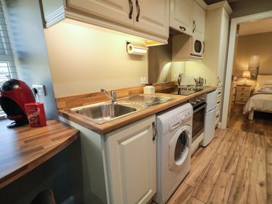 A kitchen with a sink washing machine oven mini fridge microwave and coffee machine with a view into a bedroom at Lough Island Reavy Cottage Kilcoo Mourne Mountains Newry County Down