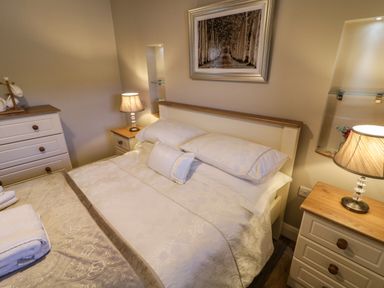 A bedroom with a bed between two bedside tables with lamps and a dresser with cups on top at Lough Island Reavy Cottage Kilcoo Mourne Mountains Newry County Down