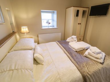 A bedroom with a bed covered in white linens and towels on top a lamp wardrobe and a small window with a vase of flowers at Lough Island Reavy Cottage Kilcoo Mourne Mountains Newry County Down