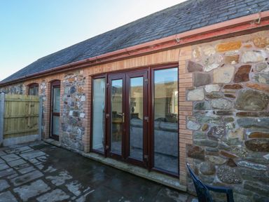 Stone exterior wall with wooden framed glass doors and windows on a paved outdoor area at The Old Well Bungalow - Ty Mawr Farm in Cardiff