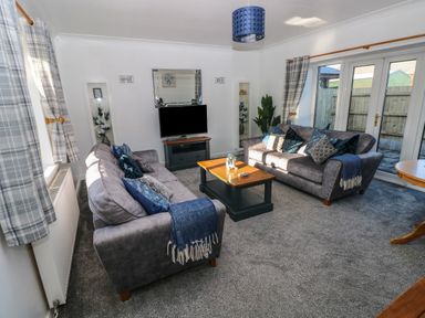A living room with two grey sofas a wooden coffee table a television on a stand and glass doors at The Old Well Bungalow - Ty Mawr Farm in Cardiff