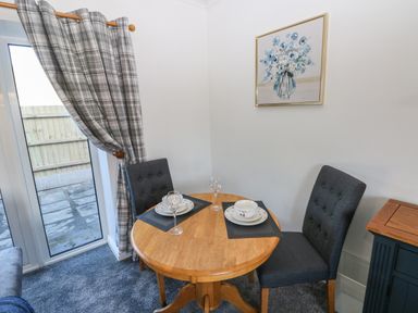 A small dining area with a round wooden table, two dark upholstered chairs, tableware, and a window with plaid curtains at The Old Well Bungalow - Ty Mawr Farm in Cardiff