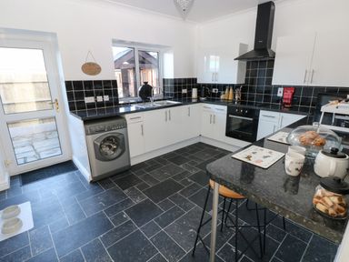 A kitchen with black tiled floors and countertops white cabinets a washing machine oven stovetop and items on the counter at The Old Well Bungalow - Ty Mawr Farm Cardiff