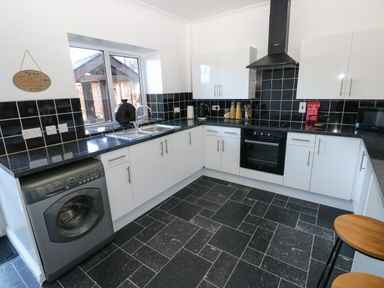 A kitchen with white cabinets black countertops a washing machine and a stove at The Old Well Bungalow - Ty Mawr Farm in Cardiff