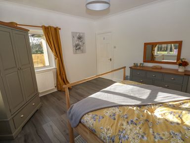 A bedroom with a wooden bed with yellow floral bedding a grey dresser with a mirror and a grey wardrobe at The Old Well Bungalow - Ty Mawr Farm Cardiff