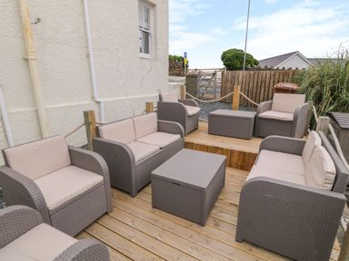 An outdoor seating area with rattan furniture and cushions on a wooden deck at Castell in Abersoch