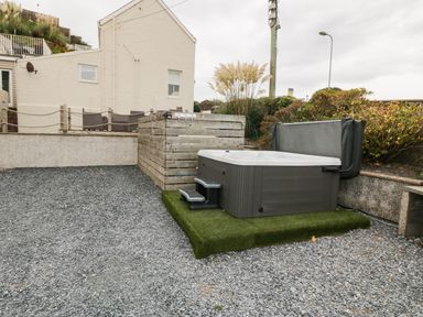 An outdoor area with a hot tub on artificial grass near a wooden fence and a building with patio furniture at Castell in Abersoch