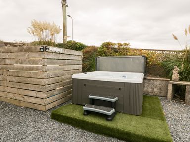 An outdoor hot tub with a cover and steps on artificial grass next to a wooden enclosure and plants at Castell Abersoch