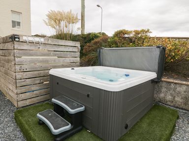 An outdoor hot tub with steps on artificial grass near a wooden structure and shrubs at Castell Abersoch