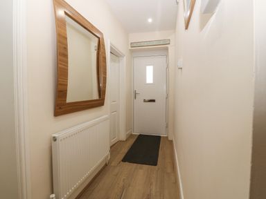 A hallway with a wooden framed mirror radiator a black mat on the wooden floor and a white door at Castell in Abersoch
