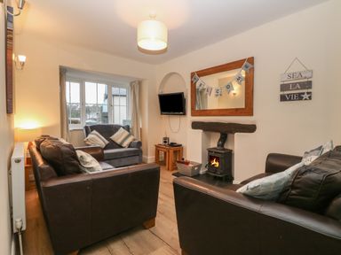 A living room with two brown leather sofas a blue armchair a wood burning stove a wall mirror and a small television at Castell in Abersoch