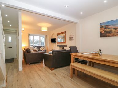 A living room with brown leather sofas a wooden dining table with bench and chair and a wall-mounted TV at Castell in Abersoch